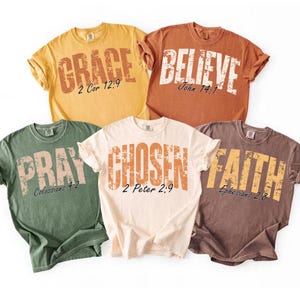May include: Five short-sleeved t-shirts in various colors: yellow, orange, green, cream, and brown. Each shirt features a large, distressed-style word: "GRACE", "BELIEVE", "PRAY", "CHOSEN", and "FAITH". Bible verses are printed below each word.