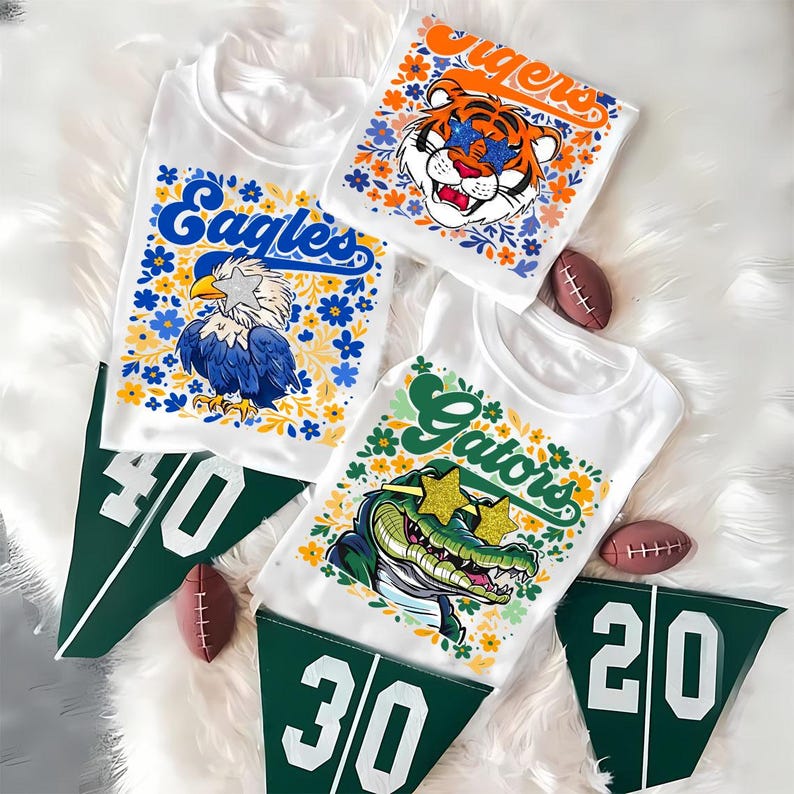 以下が含まれることがあります： チームのグラフィックが描かれた白いTシャツ。「Eagles」はワシ、「Tigers」はトラ、「Gators」はワニ。各デザインは花で囲まれています。番号が書かれた緑色のペナントとミニチュアのアメリカンフットボールも含まれています。