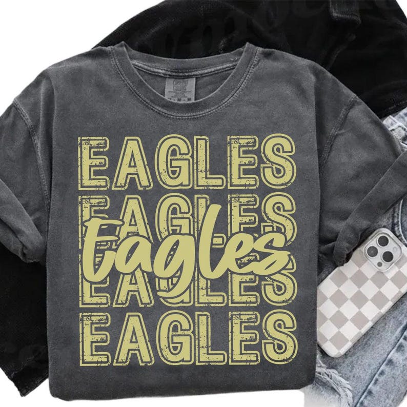 Pu&ograve; includere: Maglietta a maniche lunghe grigio scuro con la parola "EAGLES" in un motivo ripetuto in giallo chiaro. La parola "EAGLES" &egrave; impilata verticalmente, con un carattere leggermente usurato. La maglietta &egrave; piegata.