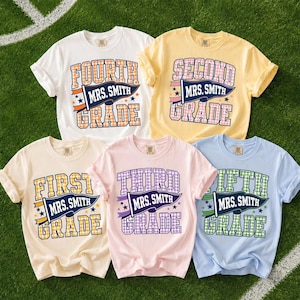 May include: Five short-sleeved t-shirts in white, yellow, cream, light pink, and light blue. Each shirt features a graphic with a pennant flag reading 'MRS. SMITH' and text indicating grade levels from first to fifth grade in a plaid pattern.