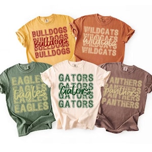Pu&ograve; includere: Cinque magliette di diversi colori con nomi di squadre stampati sopra. Le magliette sono in tonalit&agrave; di giallo, arancione, verde, crema e marrone. I nomi delle squadre includono Bulldogs, Wildcats, Eagles, Gators e Panthers.