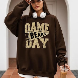 May include: A brown sweatshirt with the text "GAME BEARS DAY" in a distressed, vintage style. The graphic includes a pennant with the word "BEARS". The sweatshirt is a casual, comfortable style.