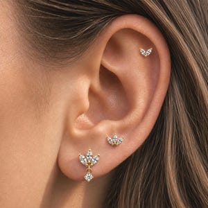 May include: Three gold-toned earrings with clear, marquise-cut and round-cut stones. One earring is a small stud with two marquise stones, another is a three-stone marquise stud, and the third is a dangling earring with three marquise stones and one round stone.