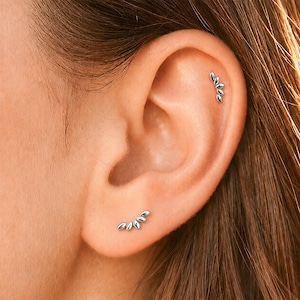 May include: A silver ear climber earring featuring a curved row of five small, polished, petal-shaped metal segments. The earring is positioned on the earlobe, while a matching silver stud earring with a similar design is worn in the upper cartilage.