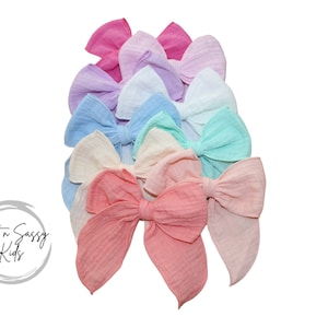 May include: A set of ten pastel-colored fabric bows. The bows are arranged in a stack, with the largest bow at the bottom and the smallest bow at the top. The bows are made of a soft, textured fabric and have a slightly ruffled appearance.