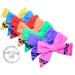 May include: A collection of colorful hair bows in a variety of shades, including yellow, blue, red, orange, green, purple, and pink. Each bow is designed to resemble a crayon, with a black wavy line detail. The bows are arranged on a white background.