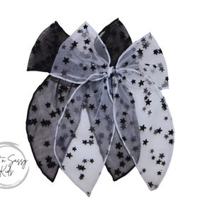May include: A black and white tulle bow with black star accents. The bow is made of two layers of tulle, one black and one white. The bow is tied in a knot in the center and has two long tails.