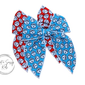 May include: A large blue and red bow with a white trim. The bow is made of fabric with a repeating pattern of the words "Thing 1" and "Thing 2".