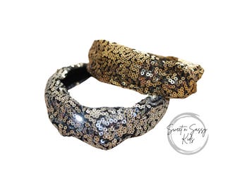 May include: Two sequined headbands, one silver and one gold, are stacked on top of each other. The headbands are wide and covered in small, shiny sequins. The background is white. The text "Sweet n Sassy Kids" is in the bottom right corner.