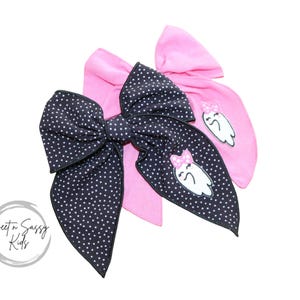 May include: Two large hair bows. One is navy blue with white polka dots, and the other is pink. The navy bow has a white ghost with a pink bow graphic. The pink bow also has a ghost graphic. The bows are for children.