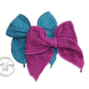 May include: Two fabric hair bows, one teal and one magenta, tied in a bow shape.