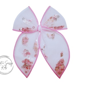 May include: A large pink and white tulle bow with pink glitter stars. The bow has a pink trim around the edges.