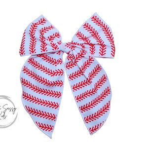 May include: A white fabric bow with a red baseball stitch pattern. The bow is tied in a knot and has two long tails.