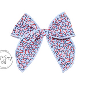May include: A white bow with a red and blue baseball heart pattern. The bow is tied in a knot and has a white edge.