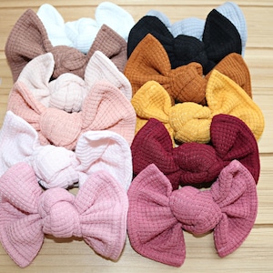 May include: A collection of ten waffle knit hair bows in various colors, including pink, brown, red, yellow, and white. The bows are arranged in a stack, with the largest bow at the bottom and the smallest bow at the top.  Sweet n Sassy Kids.