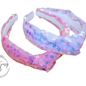 May include: Two pink and purple sequined headbands with a floral pattern. The headbands are made of a soft, stretchy material and are perfect for adding a touch of sparkle to any outfit.