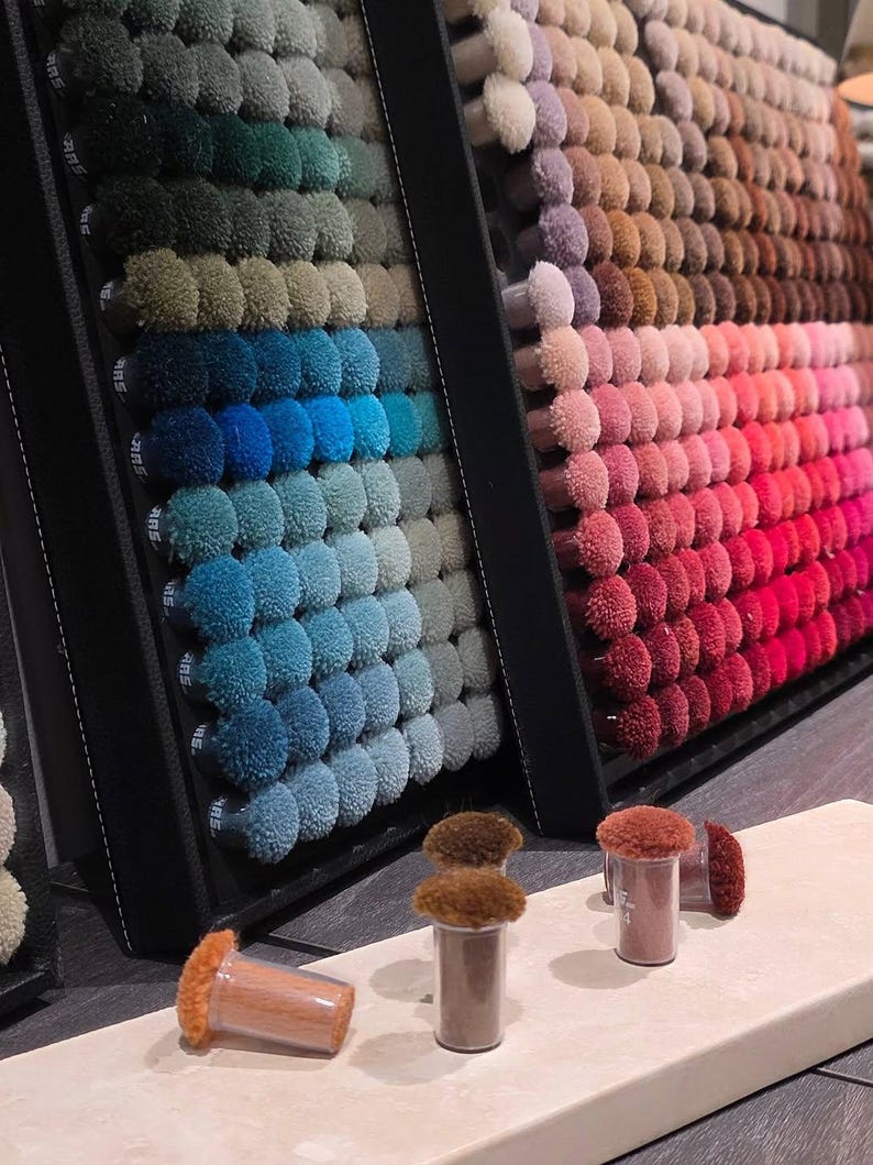May include: A display of carpet samples in various colors, arranged in a gradient from green to red. The samples are small, round tufts, and are mounted on black display boards. Several small sample containers are in the foreground.