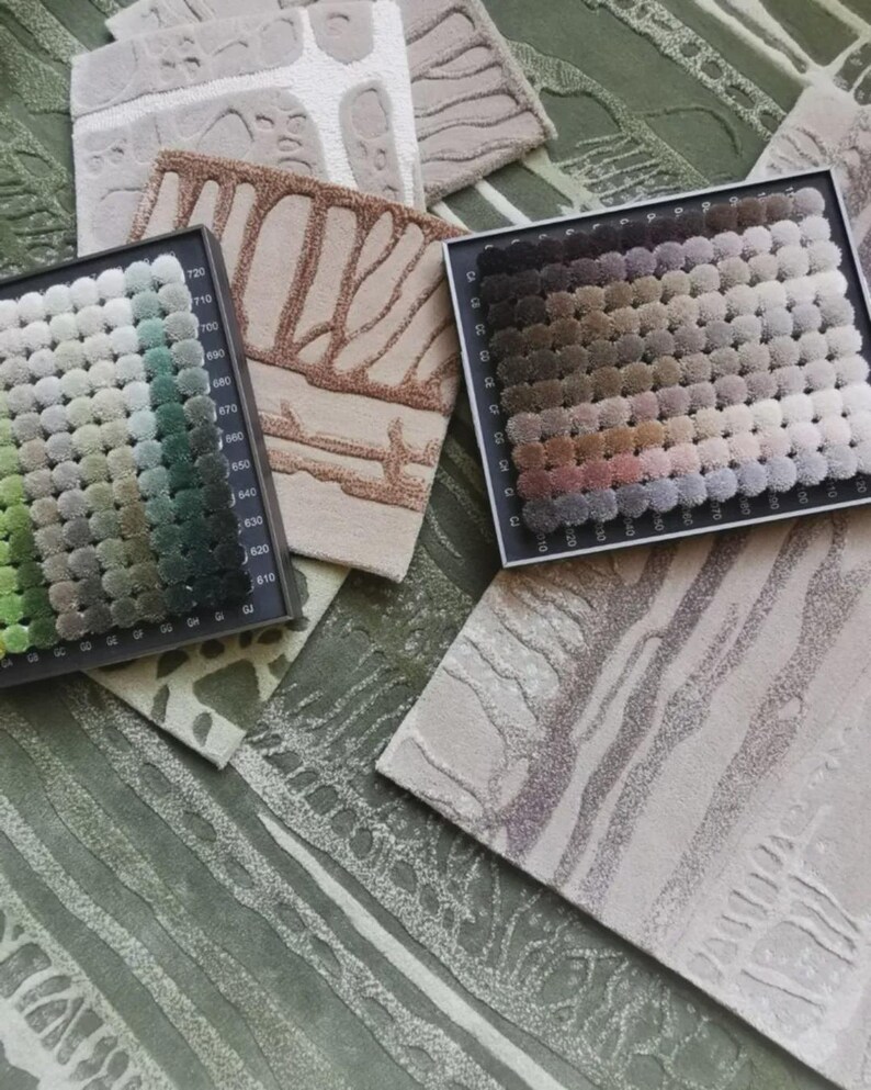 May include: An assortment of carpet samples and color swatches. The samples feature various textures and patterns in neutral tones, including beige, brown, and gray. Color swatches display a range of shades, from greens to browns, for design selection.