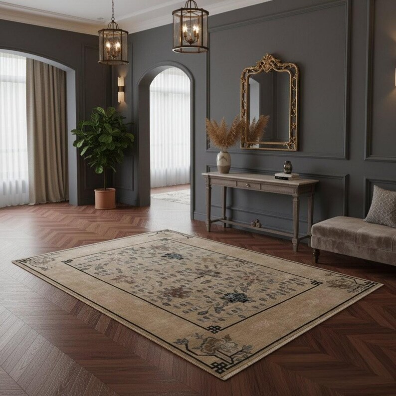 May include: A rectangular beige area rug with a floral pattern and a black border. The rug is placed on a dark wood floor in a room with dark gray walls, a mirror, and a bench.