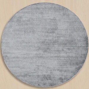 May include: A round, gray rug with a textured surface. The rug has a solid color and a simple design, suitable for various interior styles. The rug is a home decor item.