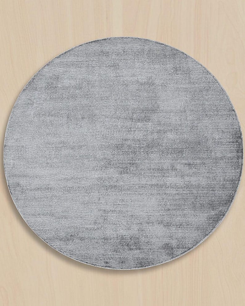 May include: A round, gray rug with a textured surface. The rug has a solid color and a simple design, suitable for various interior styles. The rug is a home decor item.