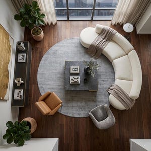 May include: An overhead view of a modern living room with a curved cream-colored sofa, a gray rug, and a square marble coffee table. Two accent chairs, one tan and one gray, are positioned near the table. Decorative items and plants add to the room's aesthetic.