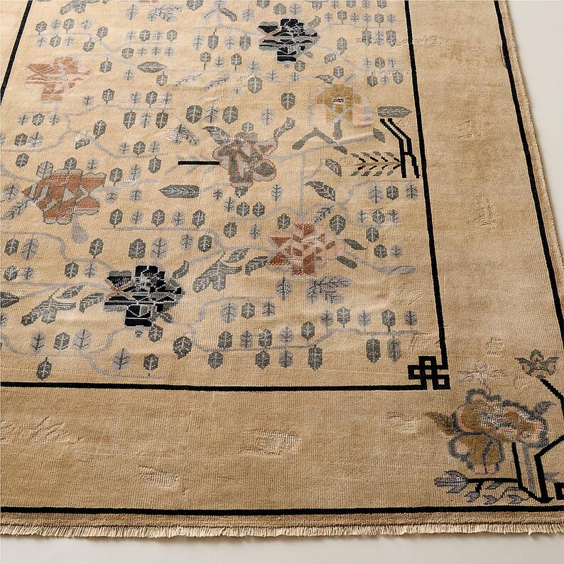 May include: Beige area rug with a floral pattern in shades of brown, gray, and black. The rug has a black border and a fringed edge. The design features stylized flowers and leaves.