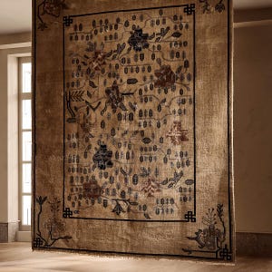 May include: A large, rectangular rug with a beige background and a detailed floral pattern in shades of brown, blue, and black. The rug has a black border and is hanging in front of a window. The rug's design includes flowers, leaves, and geometric shapes.
