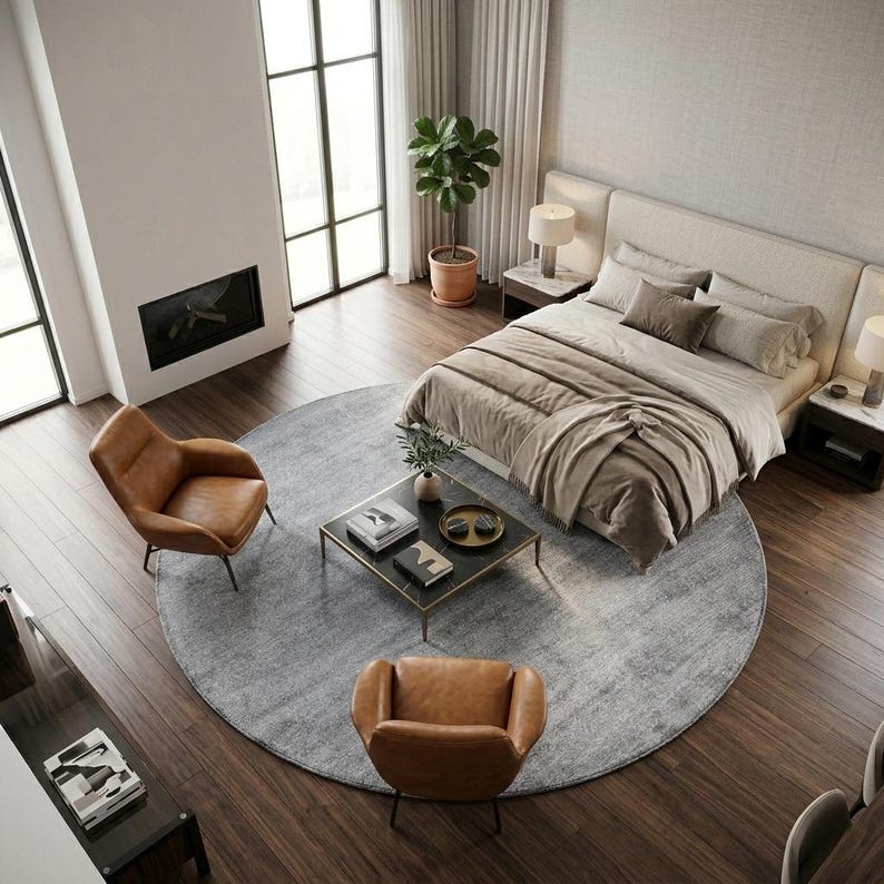 May include: An overhead view of a modern bedroom with a large bed, two brown leather chairs, and a round gray rug. A black coffee table with gold trim sits in the center of the rug. A fireplace and large windows are visible.