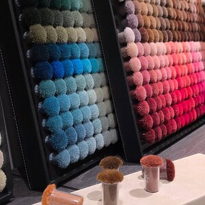 May include: A display of carpet samples in various colors, arranged in rows. The samples are small, tufted circles, showcasing a range of hues from greens and blues to pinks and reds. Several small sample containers are in the foreground.
