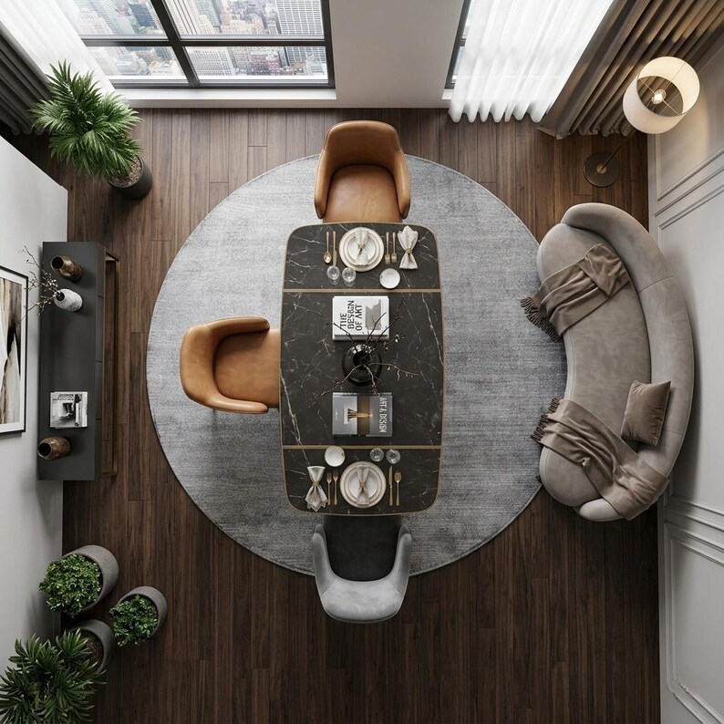 May include: An overhead view of a modern dining room. A dark marble table with gold trim is set with place settings for four. Surrounding the table are four chairs, two brown leather and two gray fabric. A gray rug sits under the table and chairs. A curved sofa is to the right.