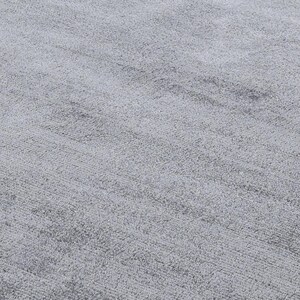 May include: Close-up of a light gray, textured rug. The rug has a soft, plush appearance with subtle variations in tone, creating a sense of depth and dimension. The fibers are densely packed, suggesting a comfortable and durable surface.