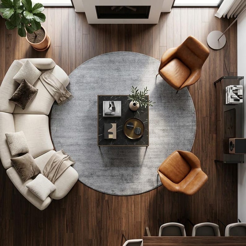 May include: An overhead view of a modern living room with a curved beige sofa, two brown leather armchairs, and a black marble coffee table. A gray circular rug sits in the center of the room on a hardwood floor.