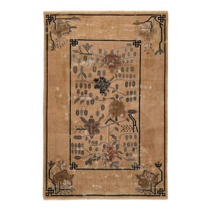 May include: A rectangular, tan-colored rug with a floral design. The rug features a central rectangular panel with a floral pattern in shades of brown, black, and gray. The border and corners have a black geometric design. The rug is likely made of woven material.