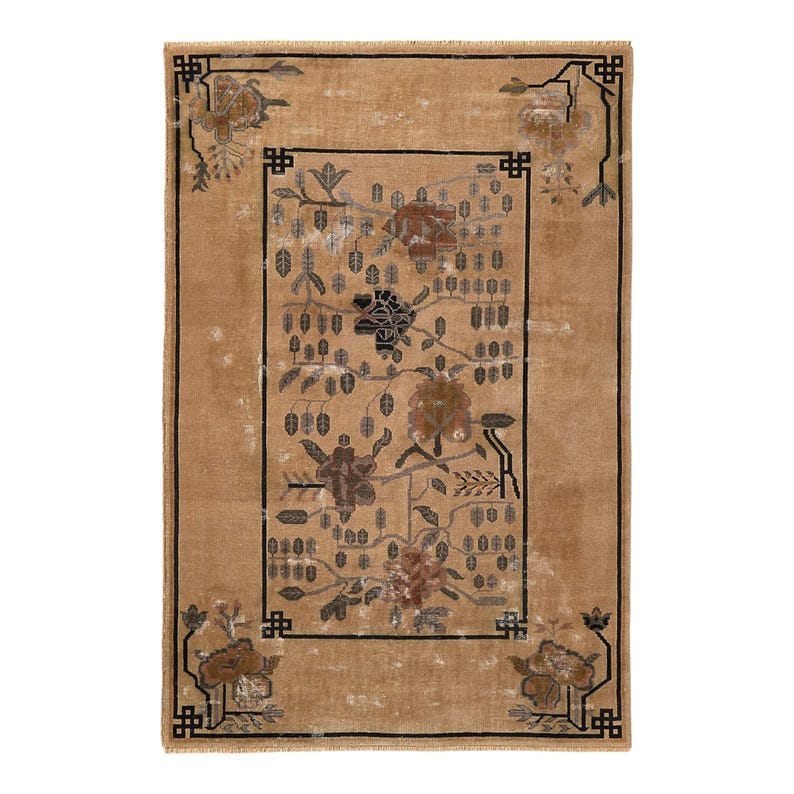 May include: A rectangular, tan-colored rug with a floral design. The rug features a central rectangular panel with a floral pattern in shades of brown, black, and gray. The border and corners have a black geometric design. The rug is likely made of woven material.