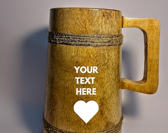 May include: Wooden beer mug with a large handle, wrapped with rope accents. The mug has the text "YOUR TEXT HERE" and a white heart graphic on the front. The mug is made of light brown wood.