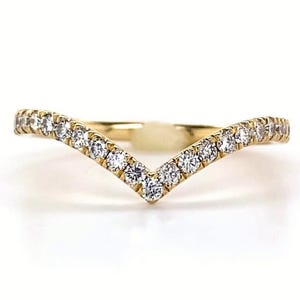 May include: A gold-colored V-shaped ring, encrusted with small, clear gemstones. The ring's design curves upwards from the center, creating a subtle arch. The ring is set against a white background, with the brand name "VEVA JEWEL" at the bottom.