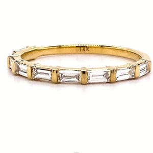 May include: A gold band ring with rectangular-cut clear stones set across the top. The ring is marked "14K" and is set against a white background. The ring is from Veva Jewel.