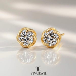 May include: A pair of gold stud earrings with a sparkling, clear gemstone center. The earrings have a twisted rope design around the gemstone. The brand name "VEVA JEWEL" is at the bottom of the image.