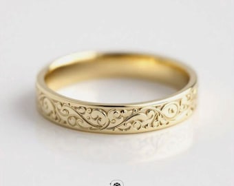 May include: A gold-colored ring with an intricate, engraved floral pattern. The ring is circular and has a polished finish. The image is well-lit, highlighting the details of the design. The ring is a piece of jewelry.