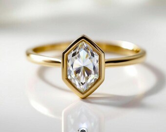 May include: A gold ring with a hexagonal-shaped diamond. The diamond is set in a gold bezel and has a brilliant cut. The ring is on a white surface, with the brand name "VEVA JEWEL" at the bottom.