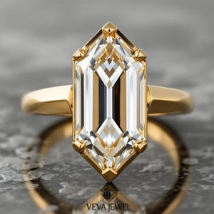 May include: A gold ring featuring a large, emerald-cut diamond. The diamond is clear with vertical facets and is set in a gold bezel. The ring band is a simple, polished gold. The brand name "VEVA JEWEL" is visible at the bottom.