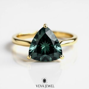 May include: A gold ring featuring a triangular, dark teal gemstone. The gemstone is faceted, displaying a starburst pattern. The ring has a simple, polished gold band and is set with three gold prongs.