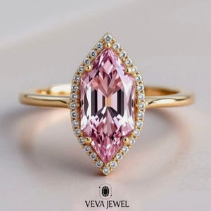May include: A gold ring featuring a large, pink marquise-cut gemstone surrounded by a halo of small, clear diamonds. The ring's band is a simple, polished gold. The brand name "VEVA JEWEL" is at the bottom.
