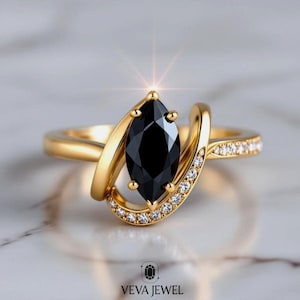 May include: A gold ring featuring a marquise-cut black gemstone, accented with small, clear gemstones along the band. The ring has a unique, flowing design with the brand name "VEVA JEWEL" at the bottom.