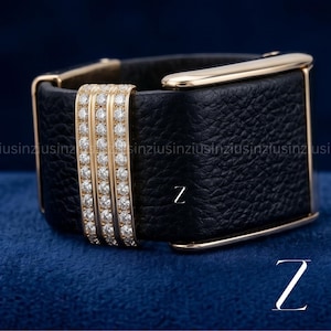 Puede incluir: Una pulsera de cuero negro con detalles dorados. La pulsera presenta tres bandas verticales doradas incrustadas con pequeños diamantes. La letra "Z" es visible en blanco en la pulsera y en el fondo.