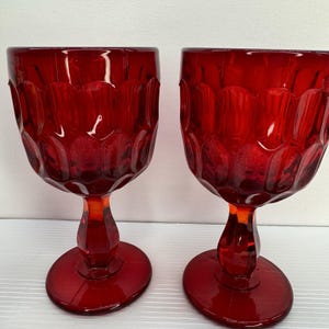 May include: A pair of ruby red goblets with a textured, scalloped pattern on the bowl. The glasses have a rounded base and a stem. The glassware is likely vintage and suitable for serving drinks.