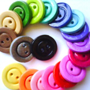 May include: A rainbow assortment of colorful buttons with two holes each. The buttons are arranged in a circle with the colors transitioning from green to purple.