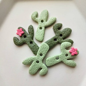 Peut inclure: Plusieurs boutons en forme de cactus dans des tons de vert, avec une surface texturée et deux trous de couture. Certains boutons présentent une petite fleur rose. Idéal pour les projets de couture.
