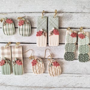 Pode incluir: Um conjunto de 10 brincos feitos à mão de argila polimérica com vários desenhos de abóbora. Os brincos são em tons de verde, marrom e branco com padrões de xadrez e bolinhas.